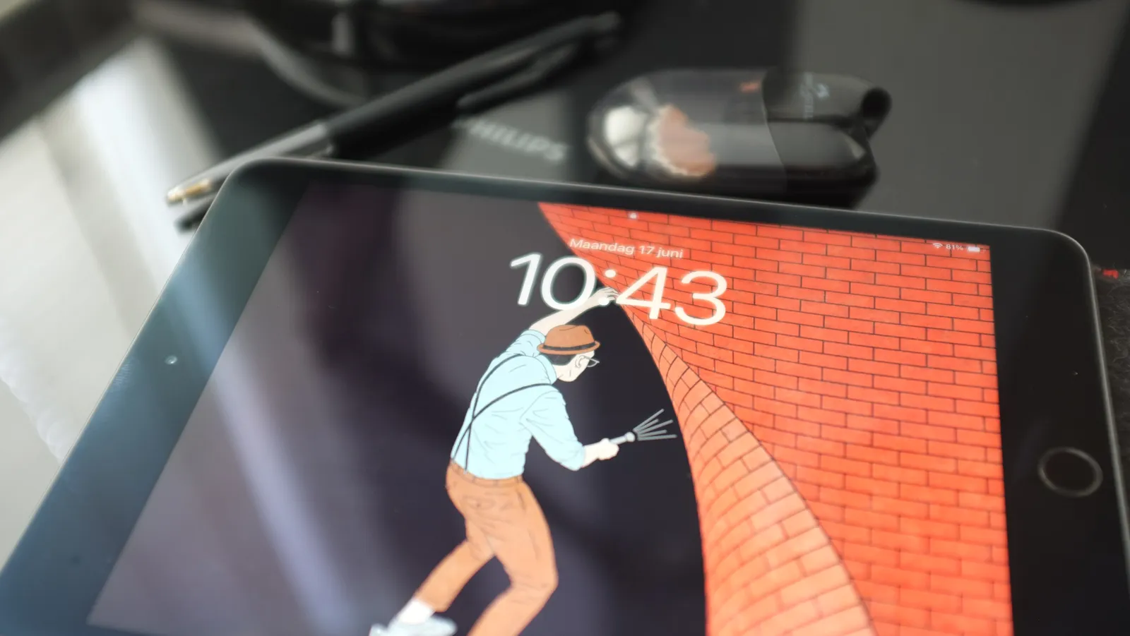 On an ipad there’s a drawing of someone shining a torch behind a brick wall with one hand. With the other hand they lift up the brick wall as if it is a sheet. The time is shown on this iPad as well, as 10:43.