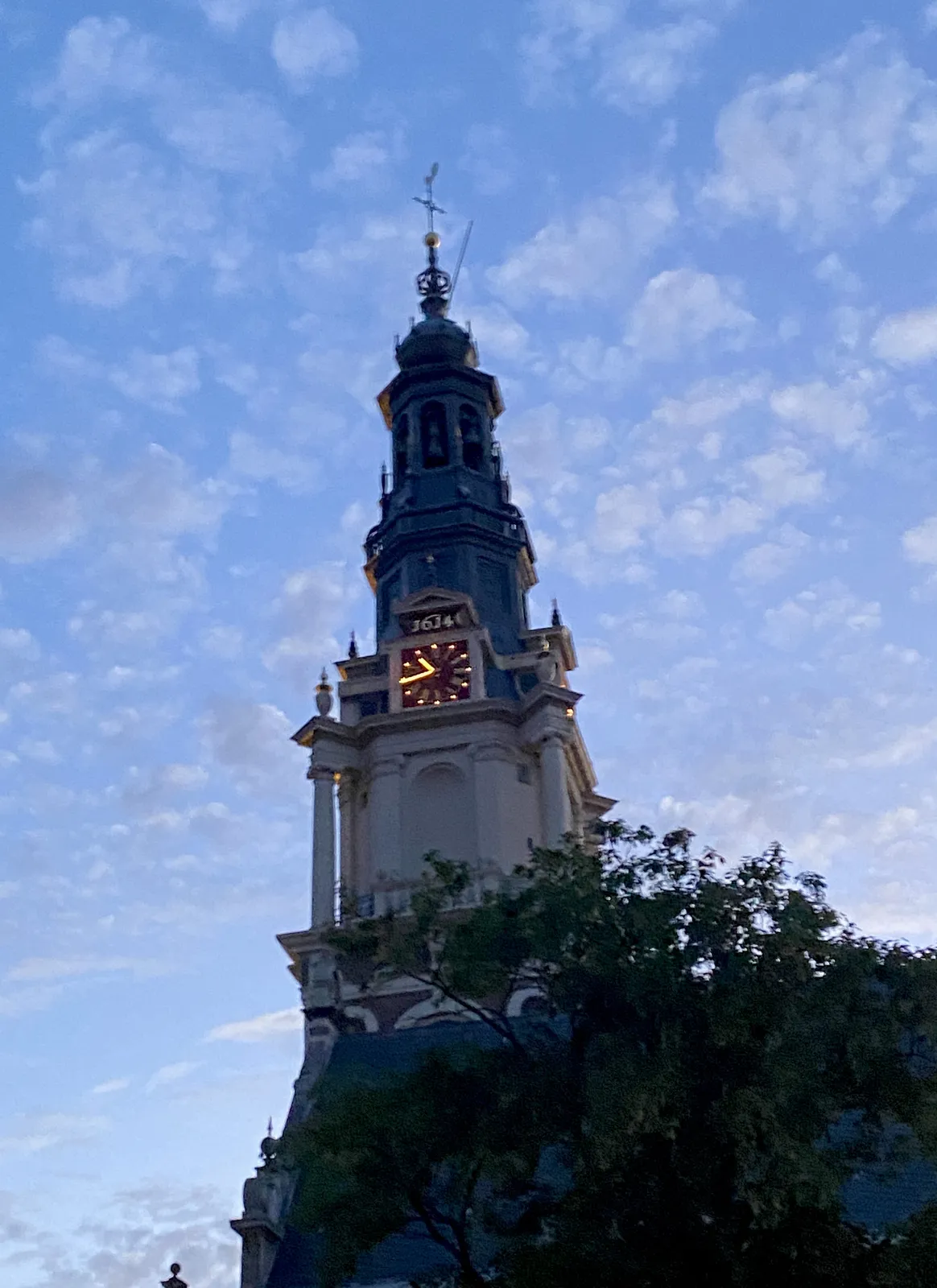 A lit clock on an old church tower. Some nice clouds behind it. It points at 16 minutes to 11.