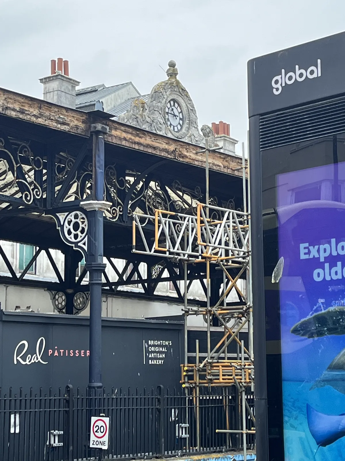 On top of an iron structure, it could be a train station, is an old clock. It points at a quarter to eleven. 