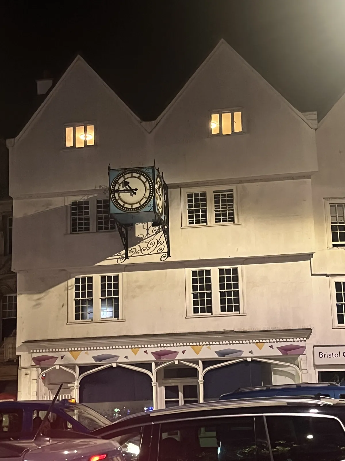 A cast iron clock, attached to the facade of a white building. The clock points at a quarter to eleven.