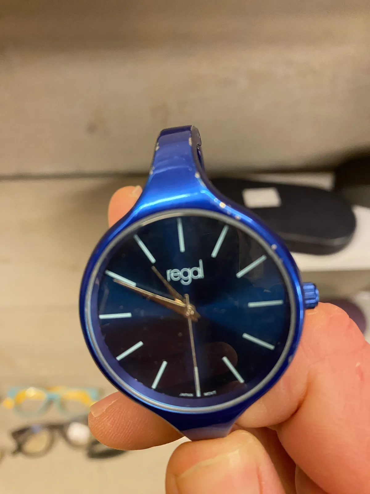 A blue wrist watch, it says Regal on the face. It points at 11 to 11.