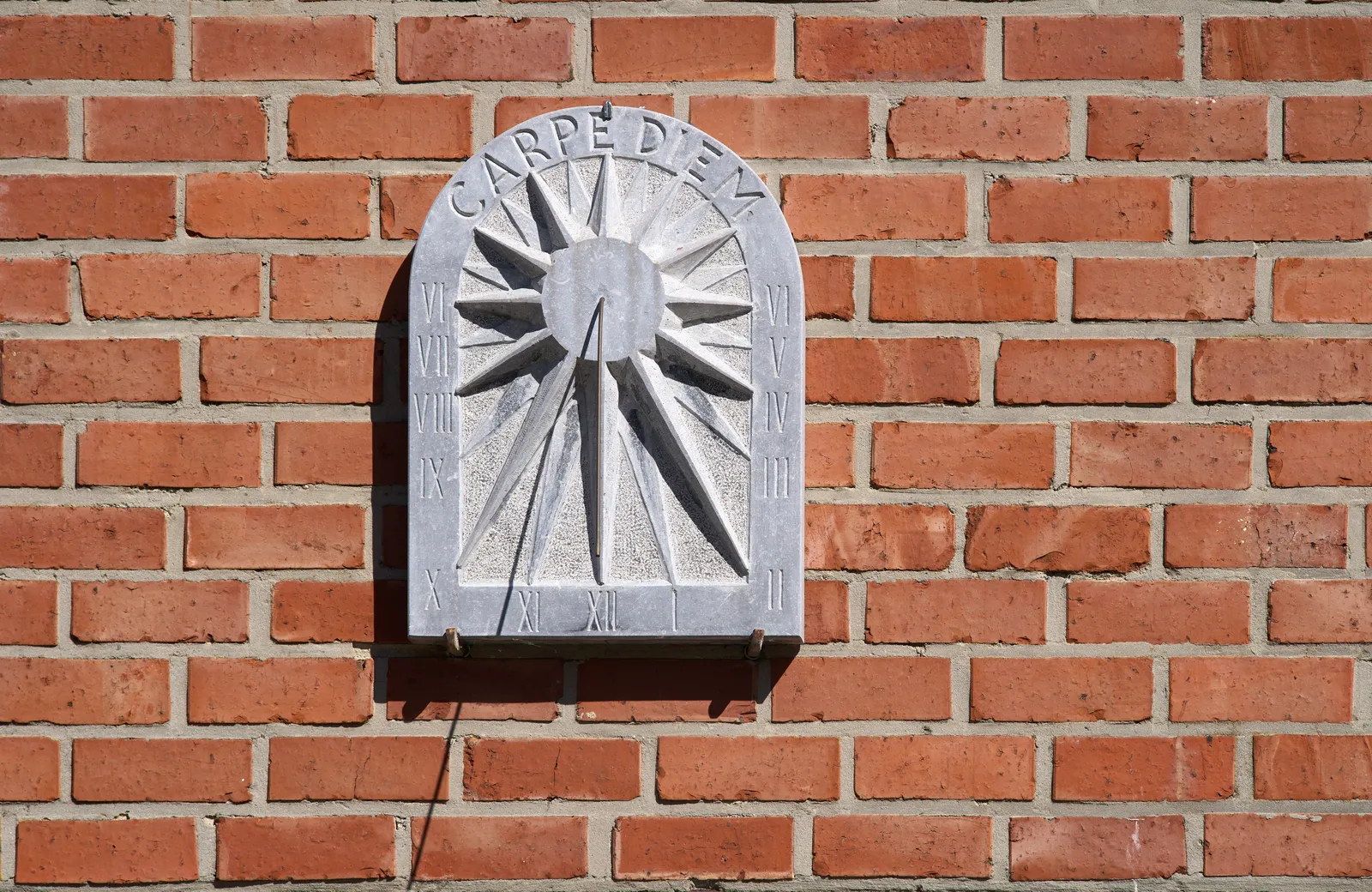 A sundial attached to a brick wall. It says Carpe Diem on top. It points at approximately ten minutes to eleven.