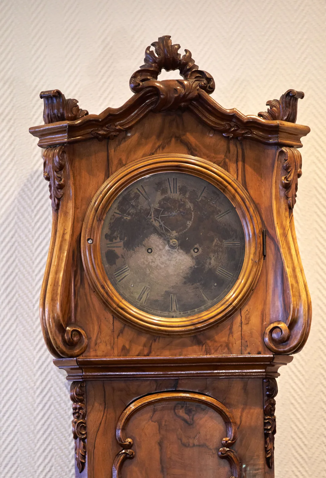 An old, wooden standing clock. The window is stained, and the hands and the face of the clock are oxidated, so it’s not easy to see the time. But it is still possible to see that it points at 8 minutes to 11.