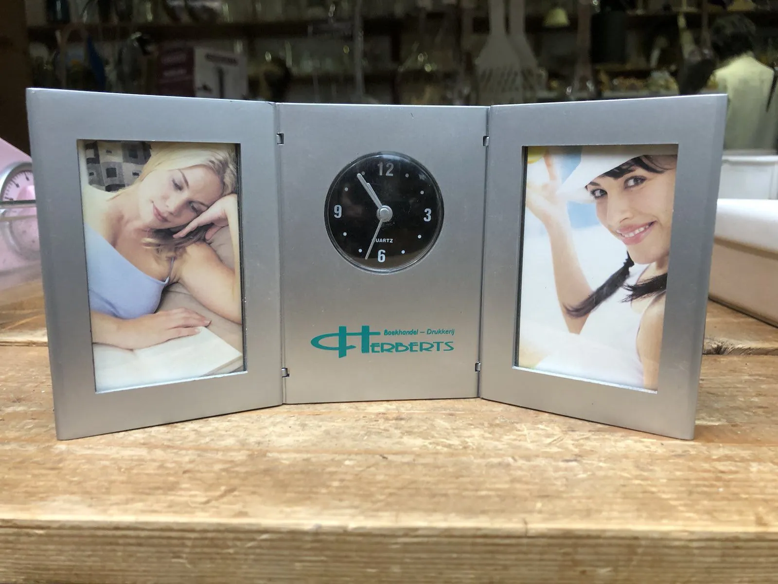 This is a picture frame for two pictures. In both there’s a smiling woman. In the middle, between these pictures there’s a clock. It points at 6 minutes to 11.