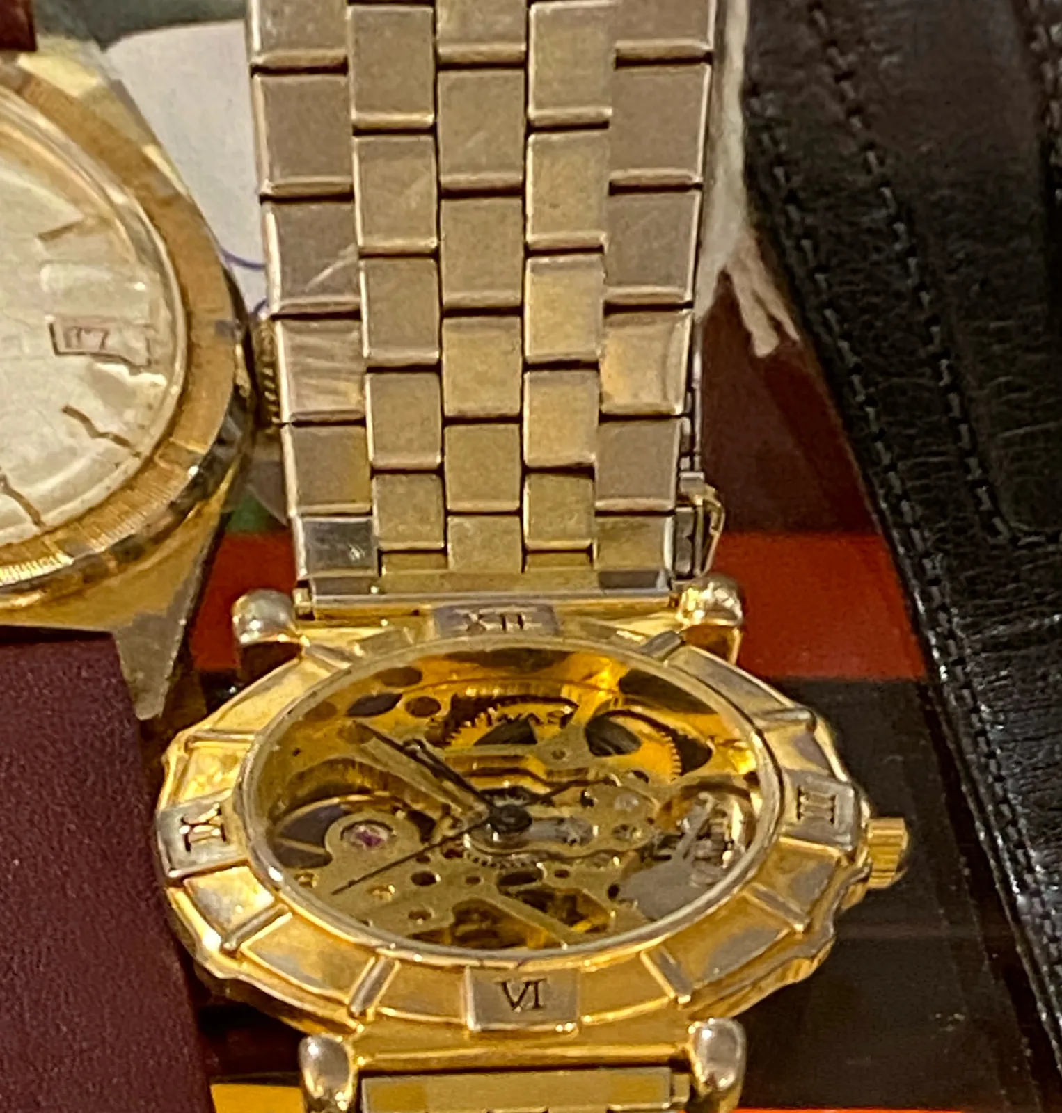 A watch, it looks gold. Its inner workings are visible. It points at 6 minutes to 11.
