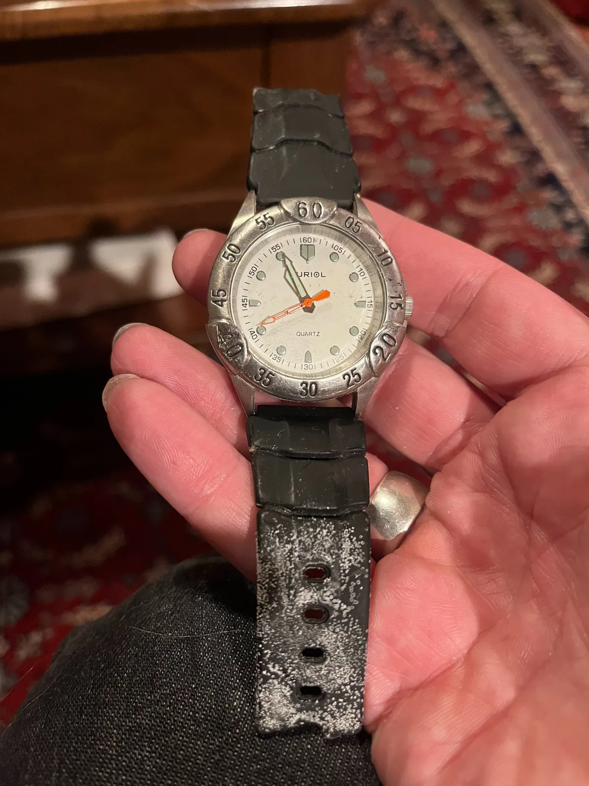 Someone is holding an old watch in their hand. In the background, blurry, an old Persian rug. The watch points at 5 to eleven.