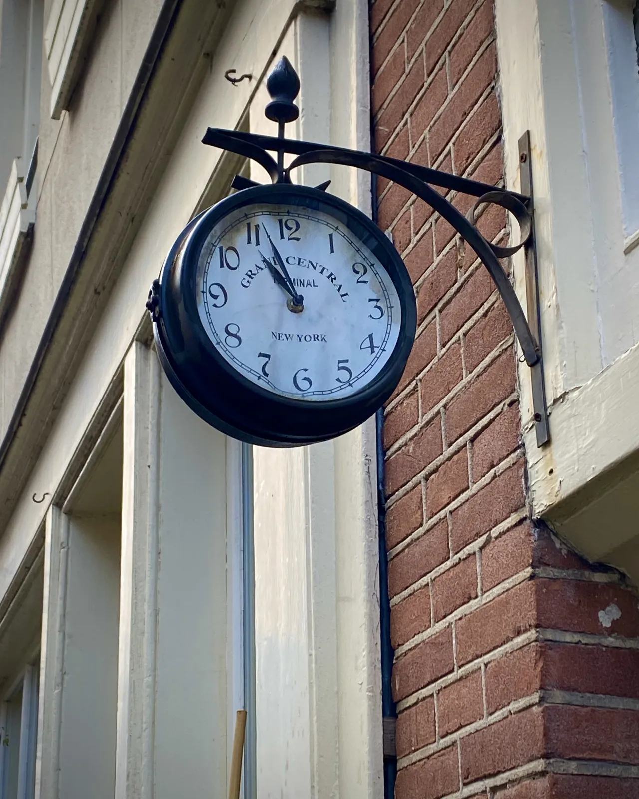 A clock attached to the facade of a building. The face of this clock is made from paper and it is bulged by the weather. On the face it says Grand Central Terminal New York, which, by the looks of the building, is probably not true. The clock points at 4 minutes to 11.