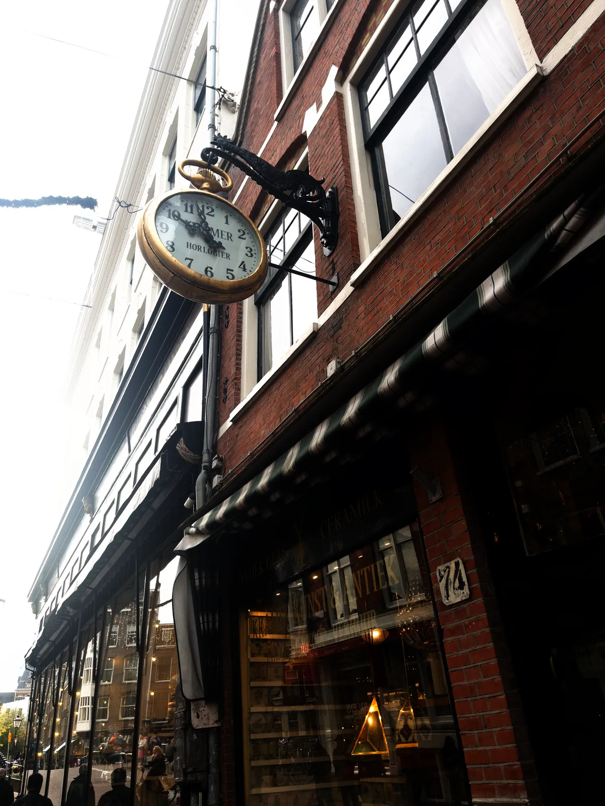Attached to the facade of this antiquities shop there’s a clock, that hangs from a cast iron rooster. The clock looks like a golden pocket watch, and it points at three minutes to eleven.