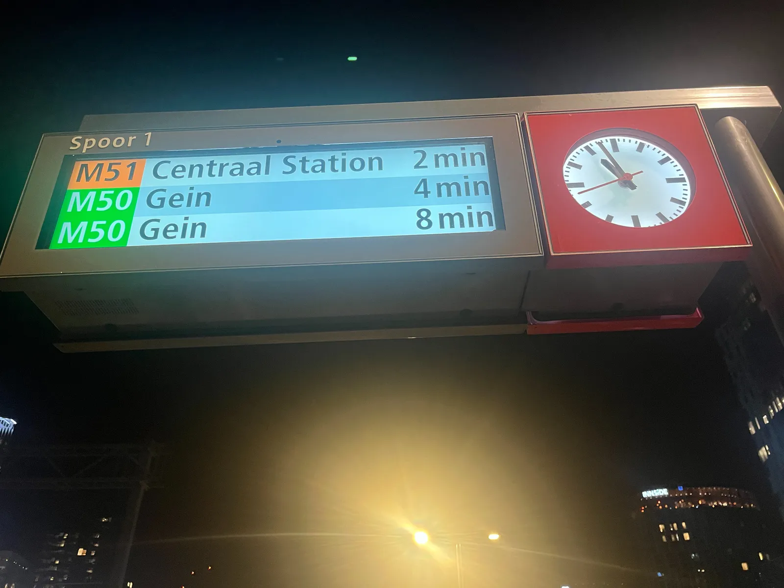 A clock on an Amsterdam metro platform. Next metro to Central Station will depart in two minutes, the next one to Gein in 4. It is three minutes to 11.