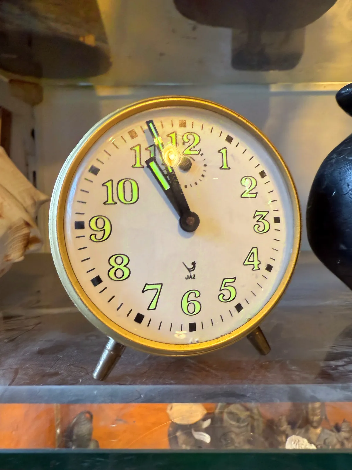 A simple, old fashioned alarm clock with fluorescent green hands and numbers. It points at three minutes to eleven.