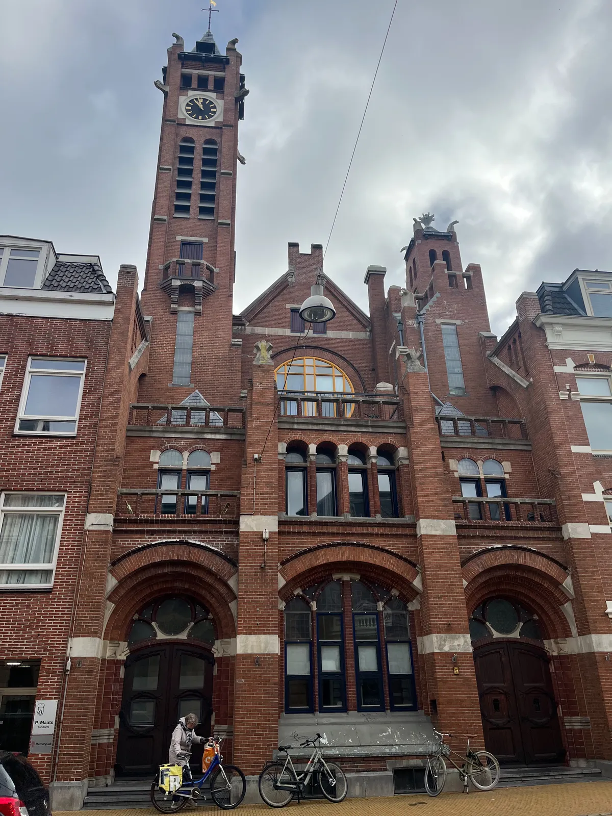 An expressive, brick church, with a high tower on it. On this tower there’s a clock which points at 2 minutes to 11