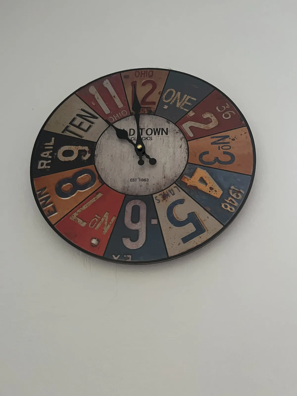 A large clock. The numbers indicating the hours are made from pictures of american licence plates. The clock points at one minute to 11.