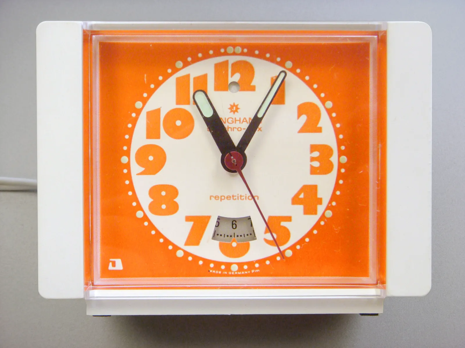 A rectangular, bright orange alarm clock with very bold numbers. It points at 5 past 11.