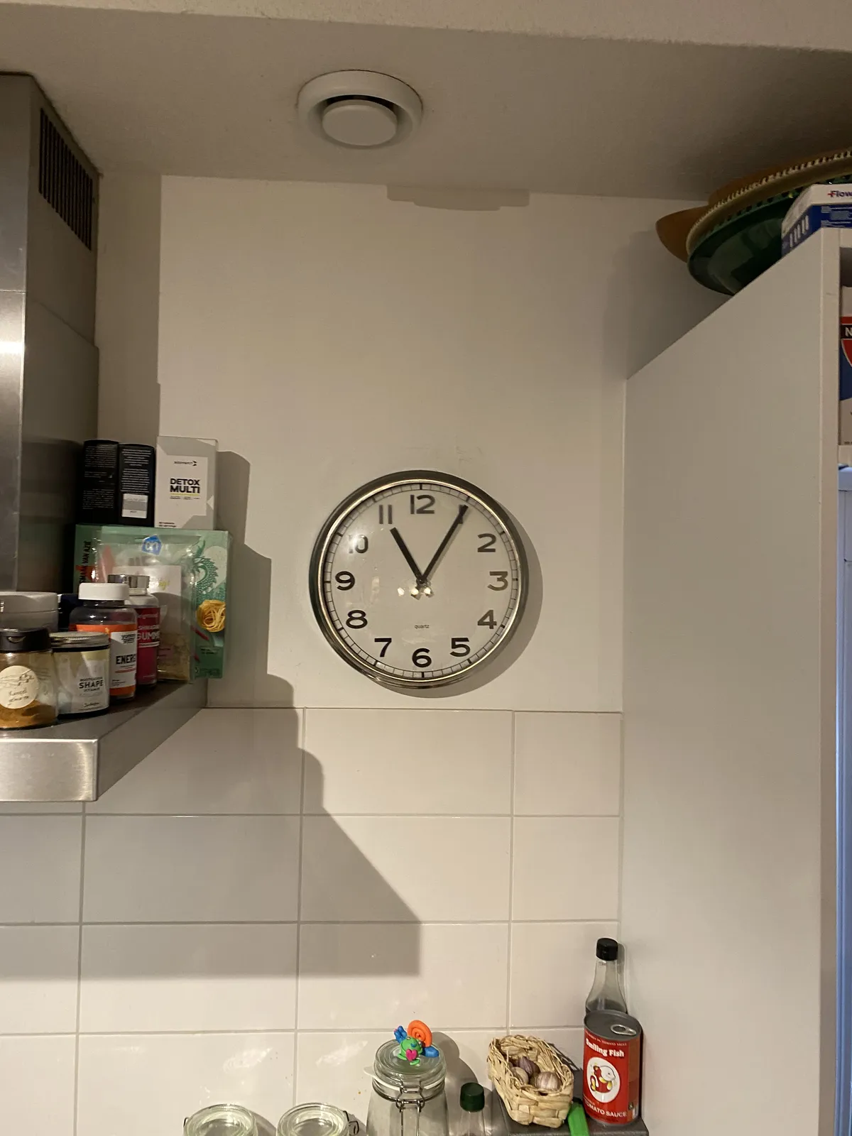 A clock on a wall in a kitchen points at 5 past 11.