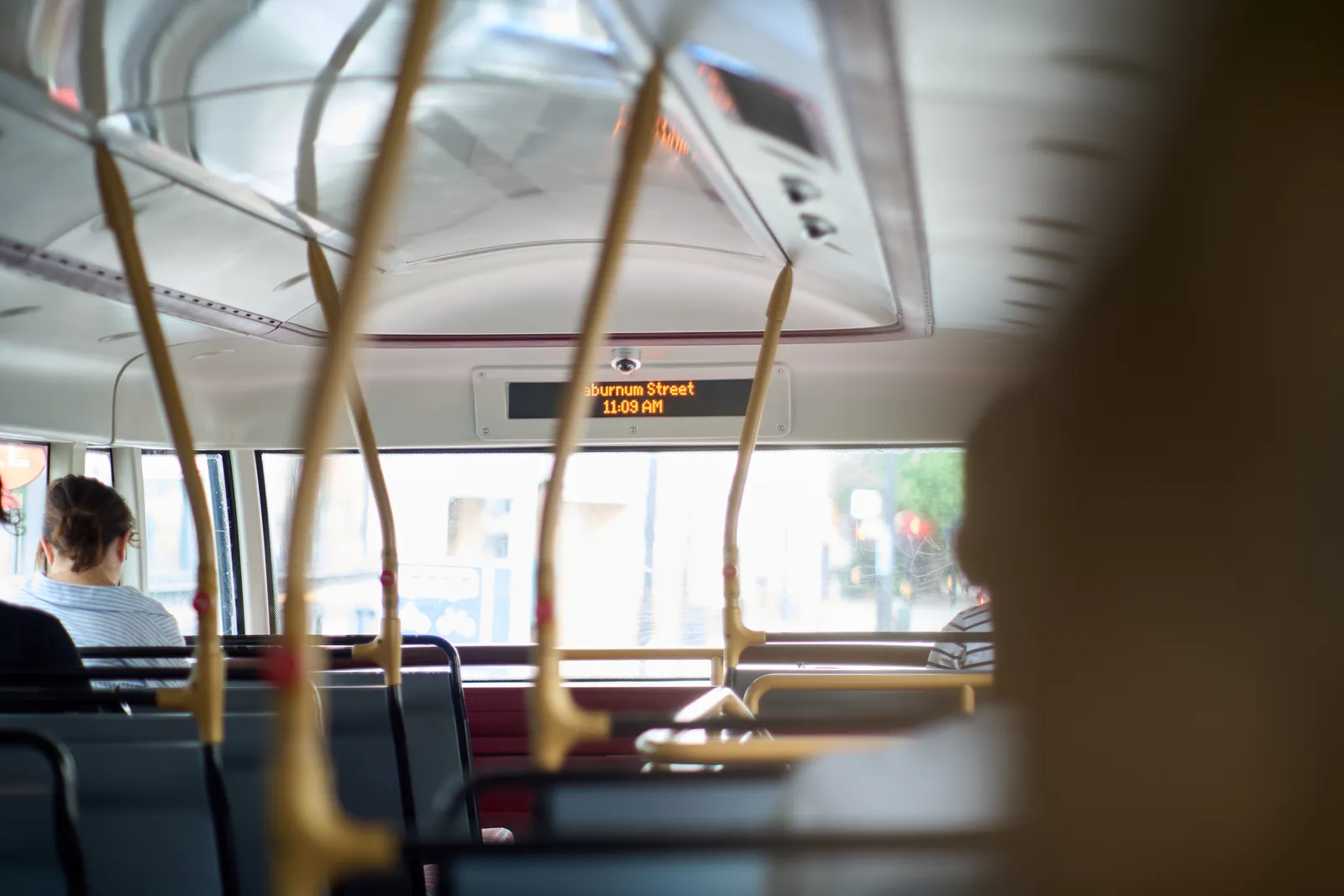 In a dubbel decker bus in London, looking from the back at an almost empty top floor. In the front, above the window there’s a digital display that says that the next stop is Laburnum Street. The time is printed below, as 11:09 AM
