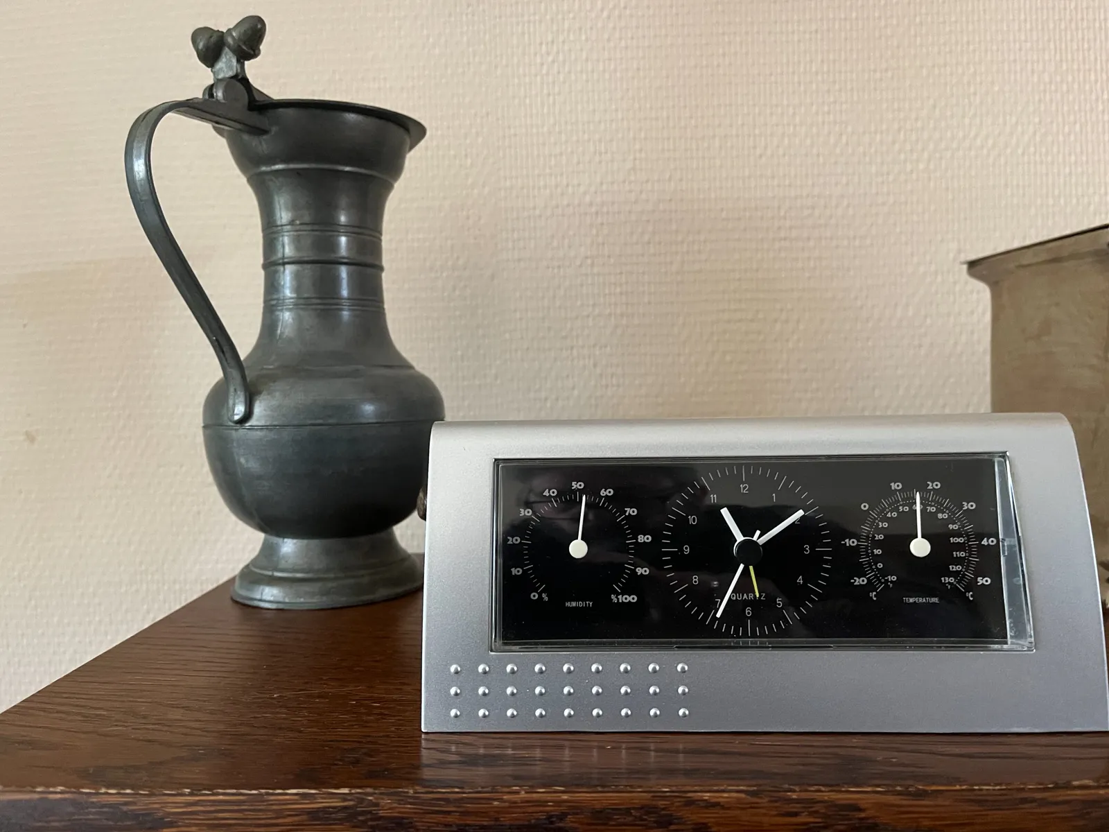 A tin can stands behind a rather modern device with three dials. The dial on the left shows the humidity, which is around 50%. The one on the right displays the temperature, which at the moment is 16 degrees celcius. And the dial in the middle is a clock which points at 9 minutes past 11.