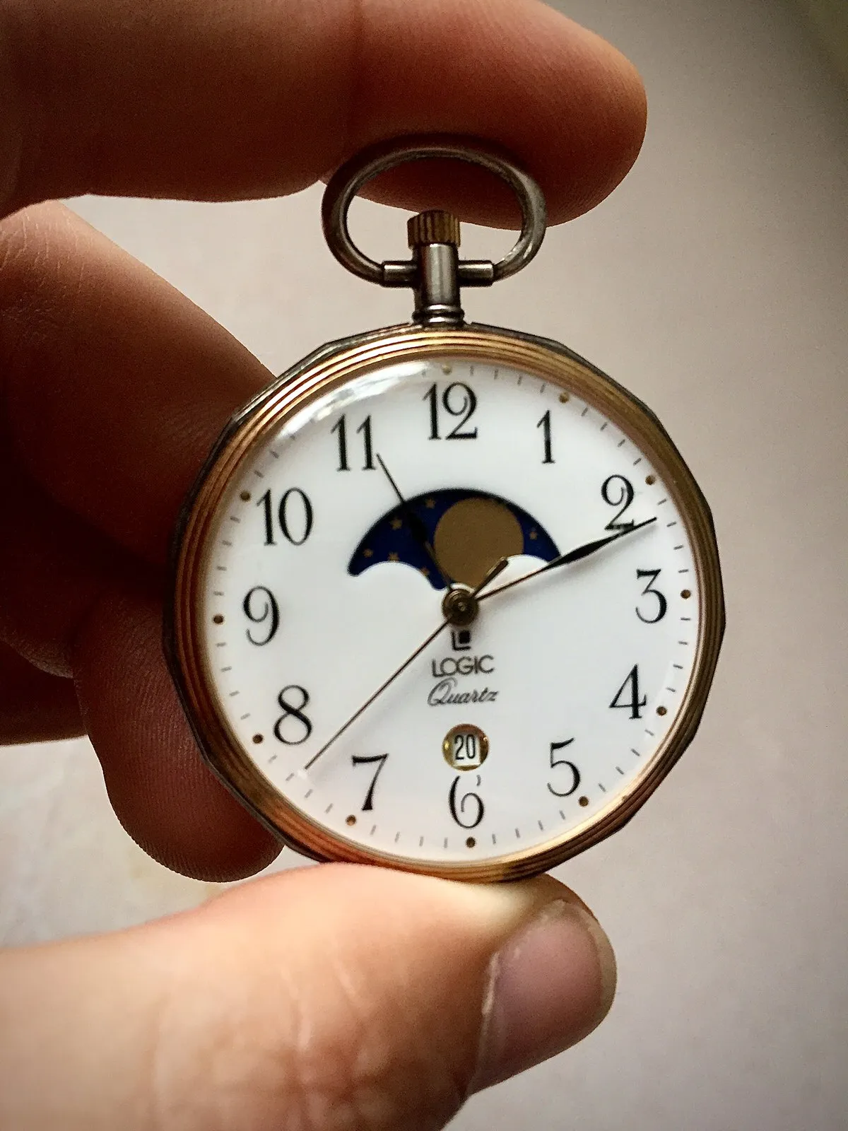 Someone holds a watch between their fingers. It points at 11 past 11.