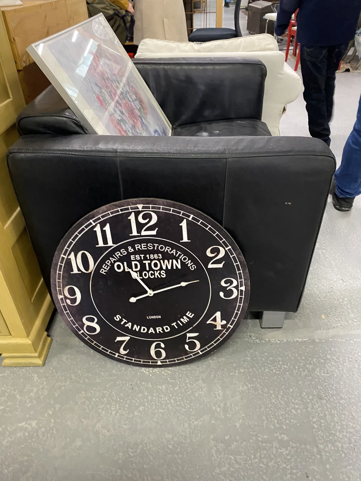 A black clock with white arms, and white text on it. It points at 13 past 11.