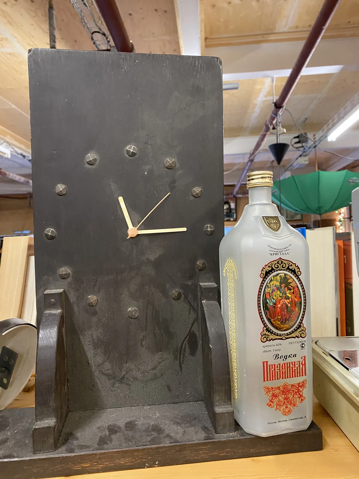 An old bookshelf clock points at 14 past 11. There’s a bottle of Vodka standing on this clock.