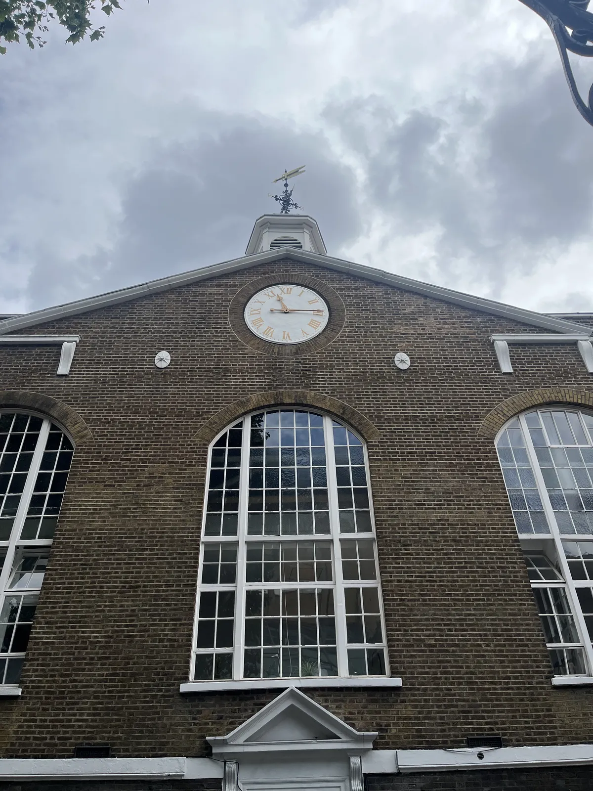 On top of a high, brick, churchlike facade, above the high windows with white frames, there’s a clock which points at 14 minutes past eleven.