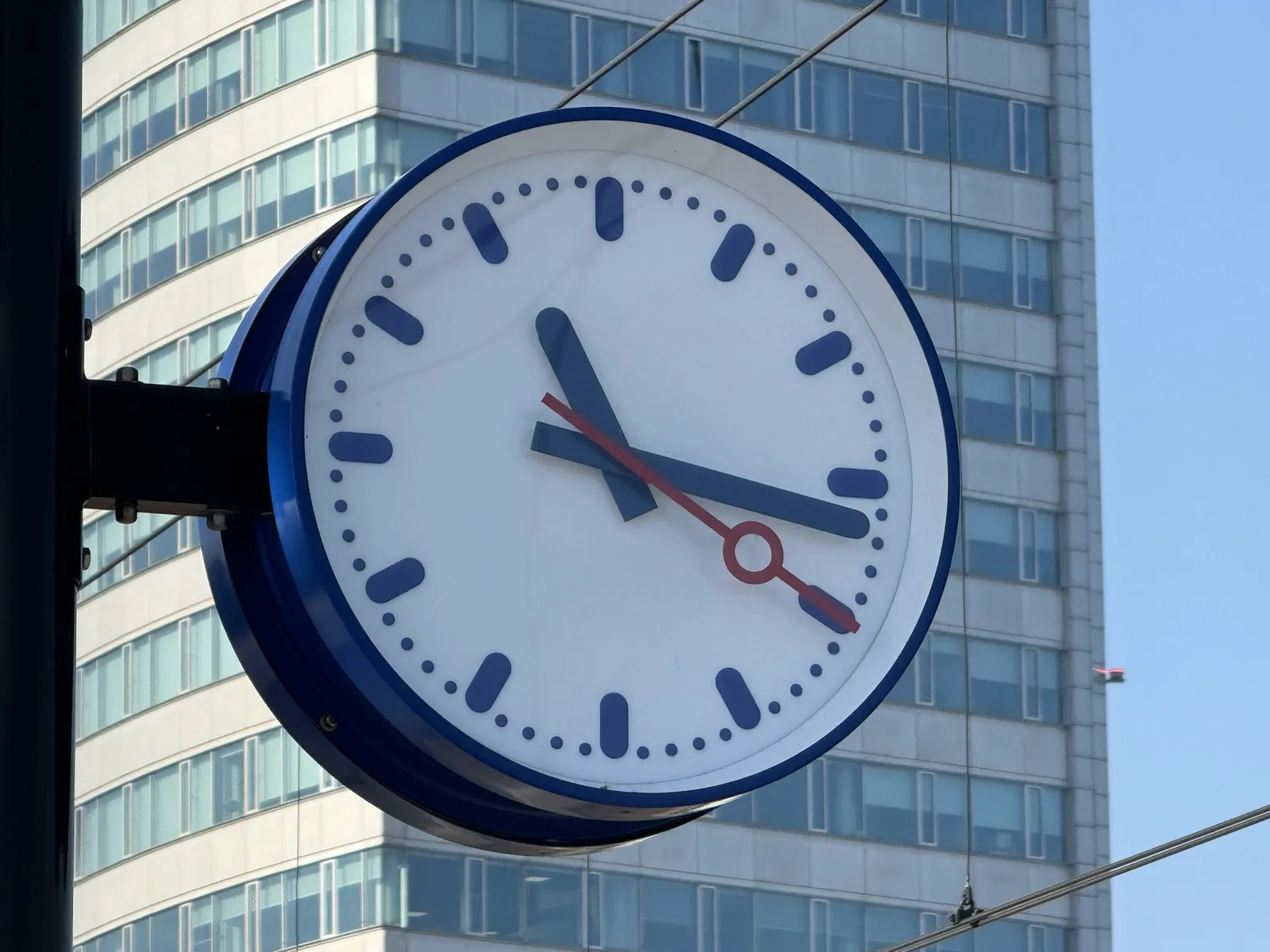 A Dutch train station clock, with in the background a high flat. The clock points at 16 minutes past 11.