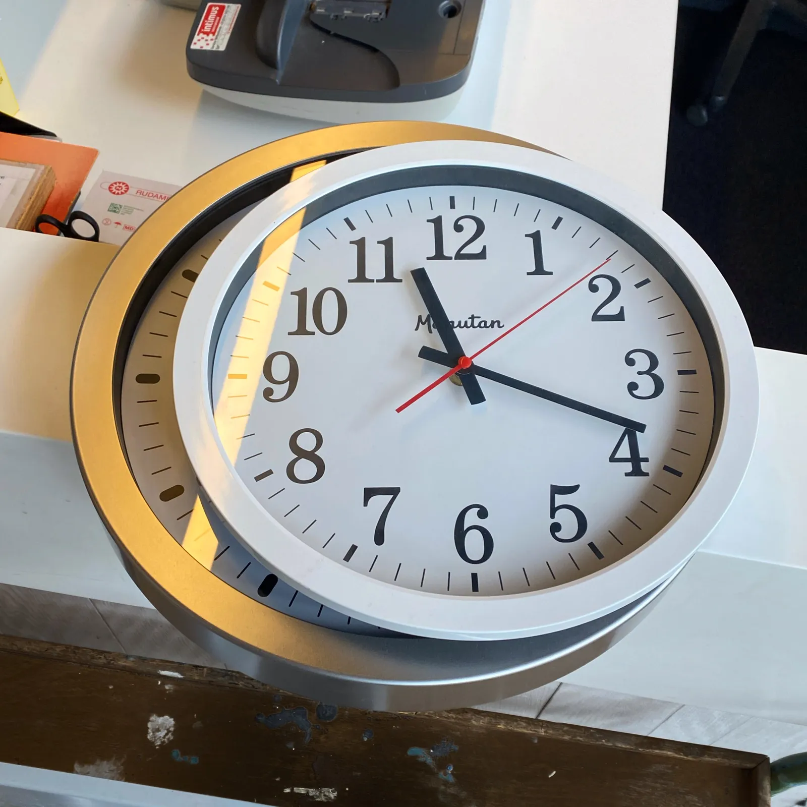 There’s a clock laying on top of a clock laying on a desk. You can only see the time on the top clock. It points at 18 minutes past 11.