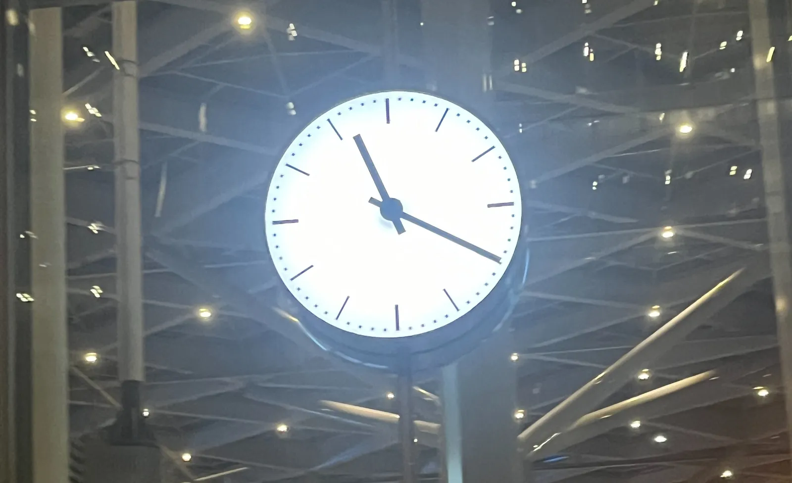 A brightly lit station clock in a glass facade. It points at 19 minutes past 11.