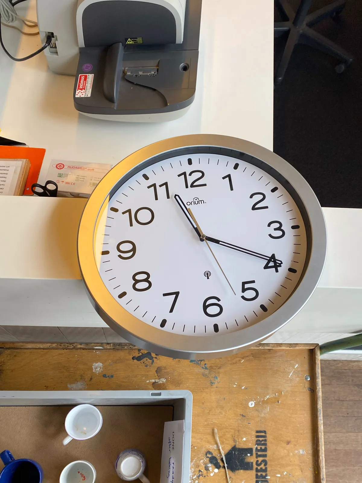 A clock laying on a desk. It points at 19 minutes past 11.