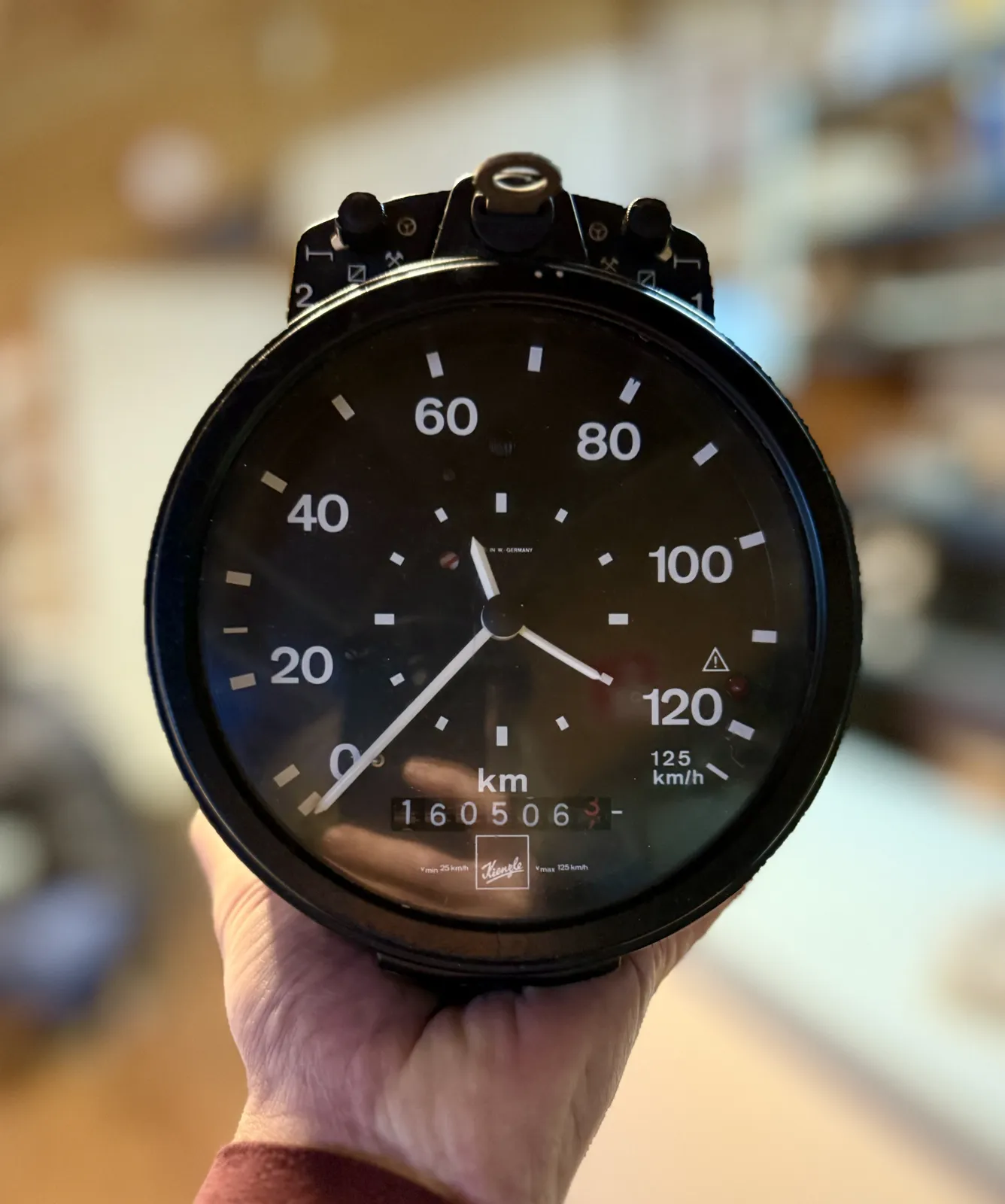 Someone is holding a large black tachometer in their hands. It indicates that they are not moving. There’s also a clock on this thing that points at 20 minutes past eleven.