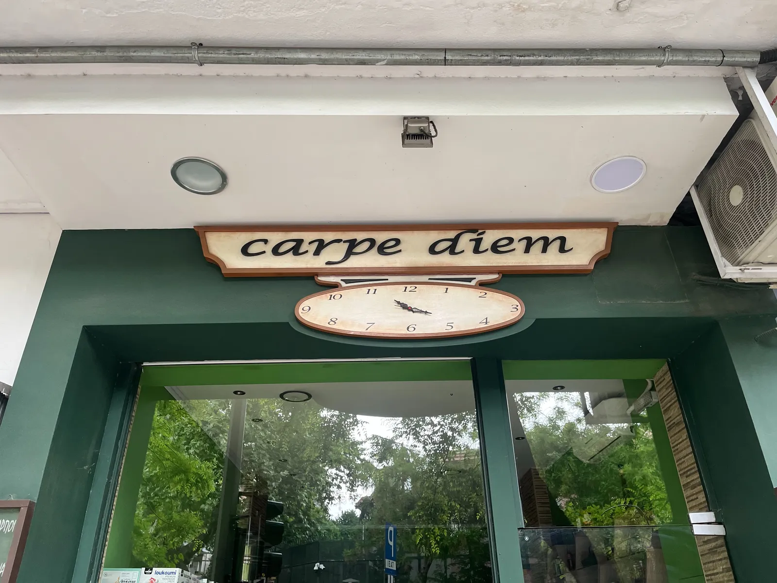 Below the sign of a shop called Carpe Diem there’s an oval shaped clock which points at approximately 21 minutes past eleven.