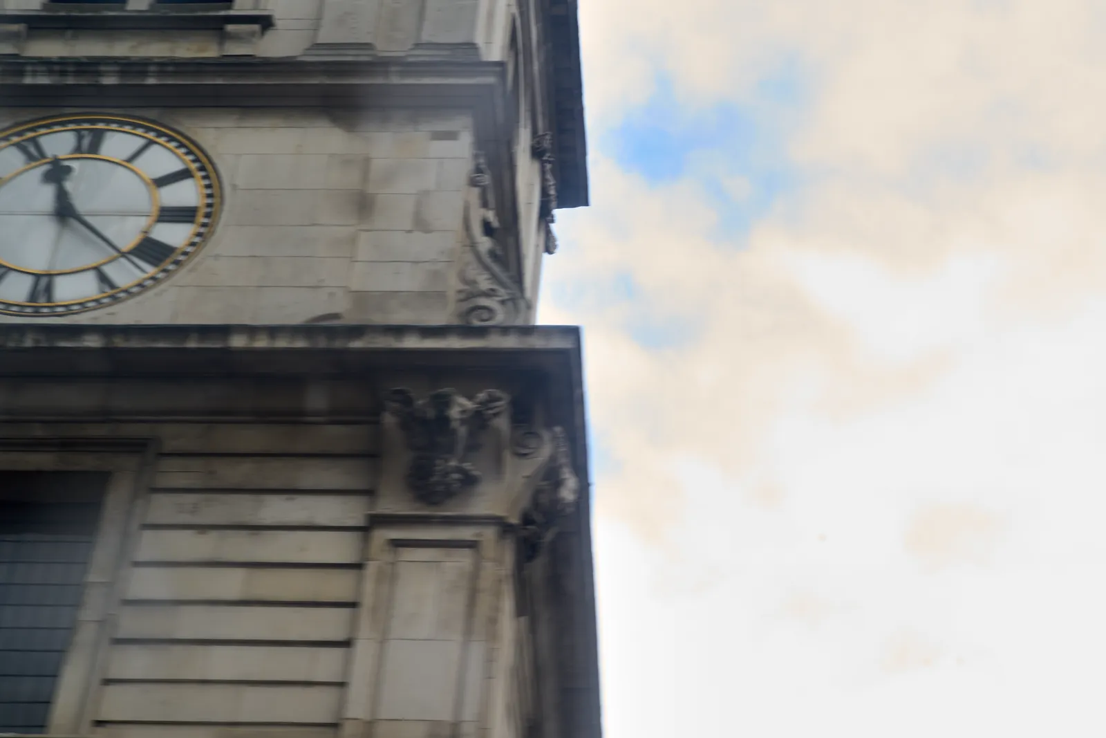 A blurry image, with on the left part of a tower with a clock on it, and on the right the sky. The image is a bit blurred by motion. The clock on the tower points at 22 minutes past eleven.