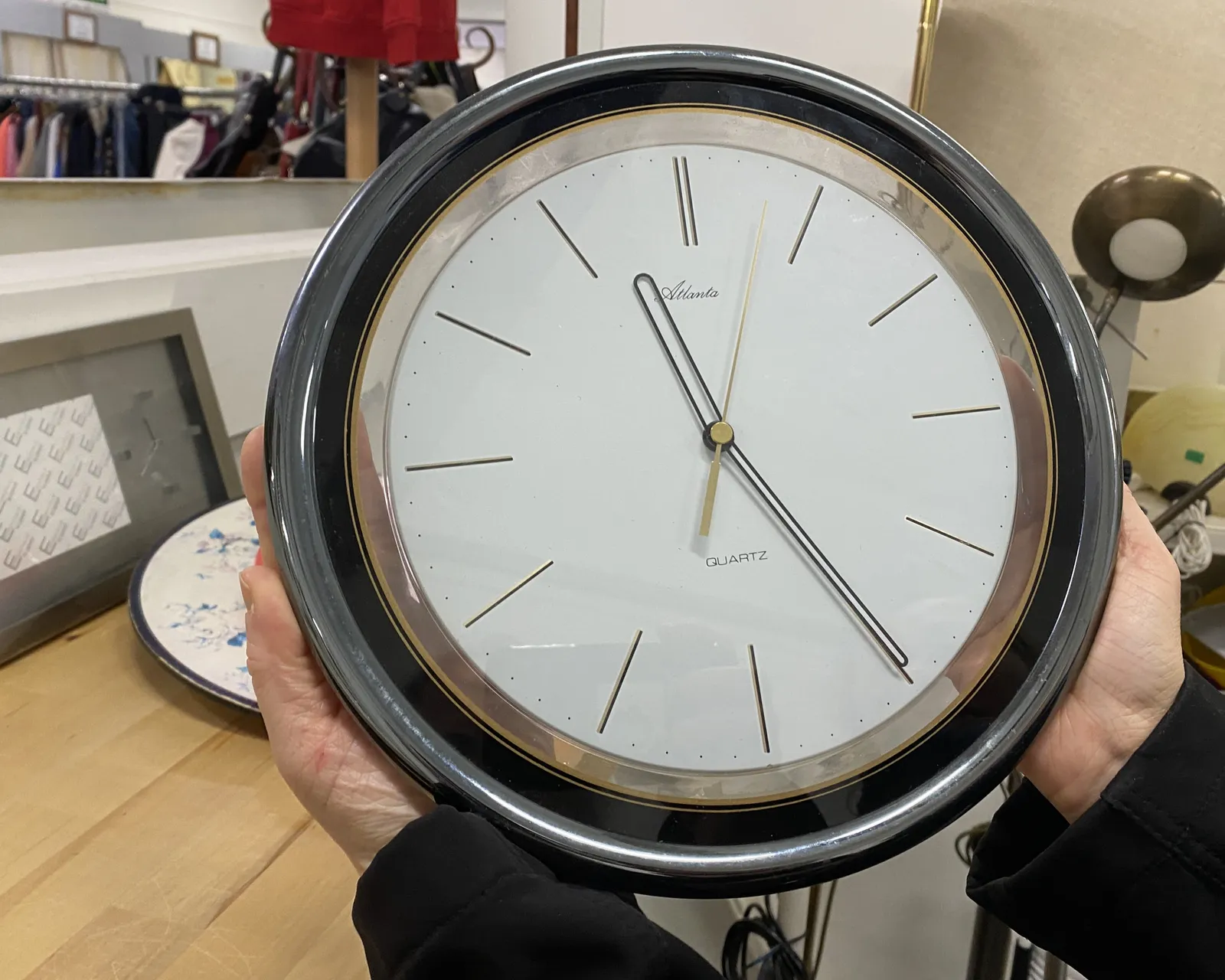 Someone is holding a shiny clock in their hands. It points at 24 minutes past eleven.