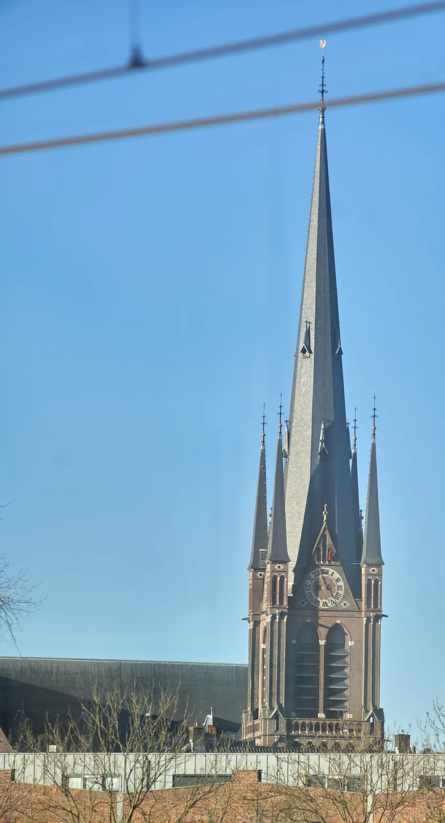 An enormous church tower on a bright, sunny day. The clock on this tower points at 27 minutes past 11.