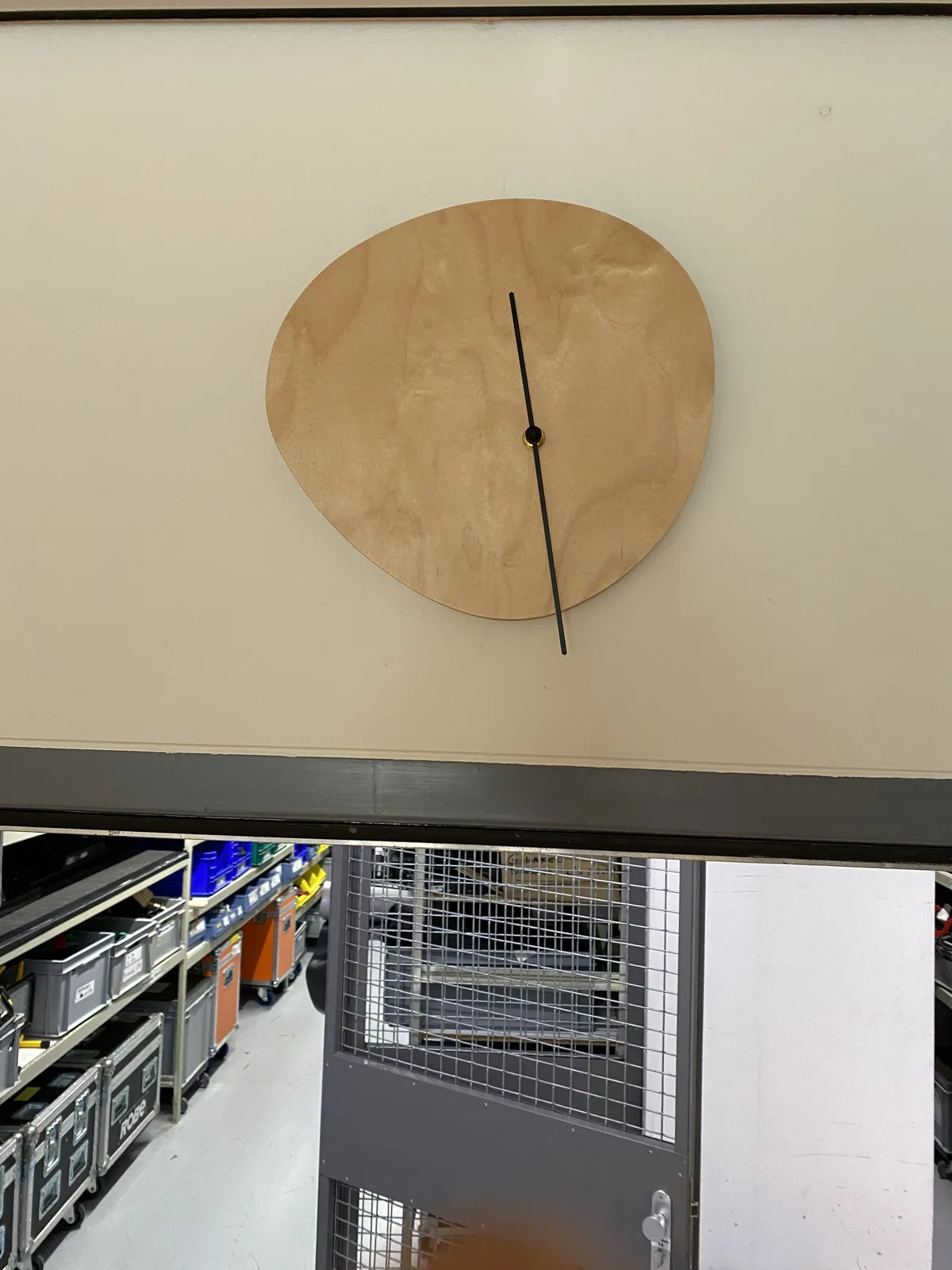A wooden clock in the shape of a blob. Its hands are placed off center. It points at approximately 28 past 11.