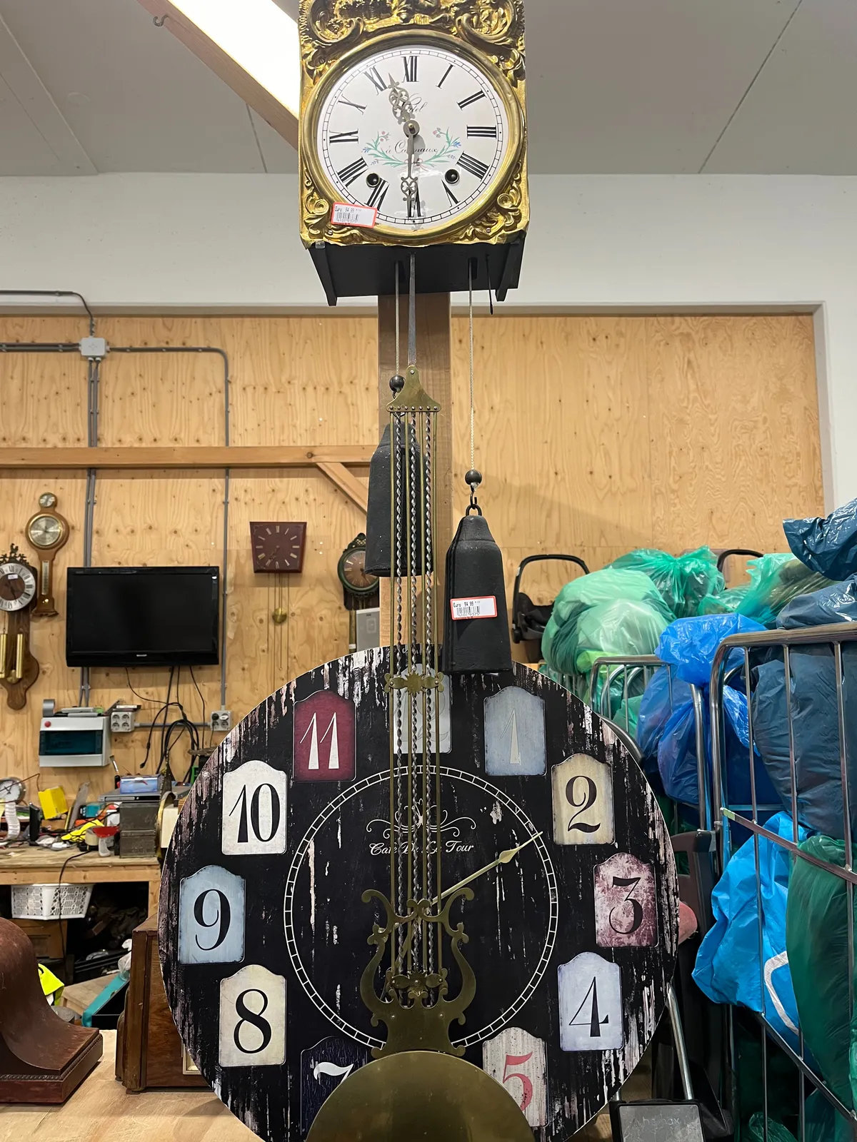 There are quite a few clocks in this picture, but on only one of them the time can be seen clearly. It is an old, golden wall clock, with two heavy weights and an enormous pendulum. This clock points at half past 11. 