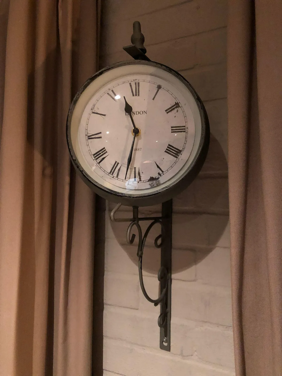 A clock, attached to a wall between some curtains. It points at 32 minutes past 11.