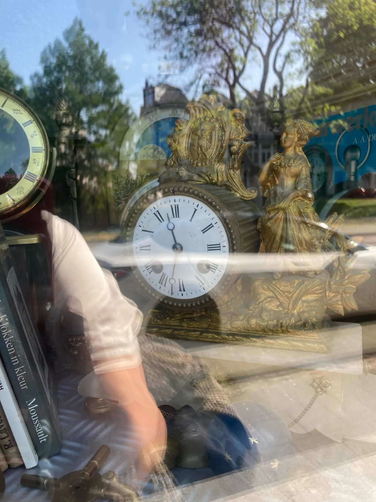 A clock behind a window. It’s richly ornamented, it even has a statue of a woman in a dress. The clock points at 11:32.
