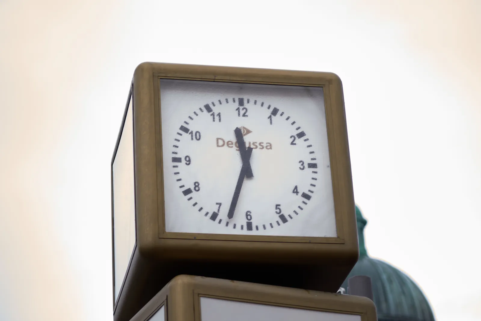 A large street clock in a brown cube. It points at 27 minutes to 12.