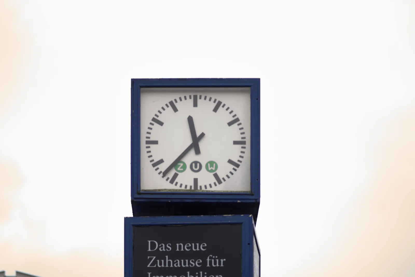 A street clock in a blue cube. It points at 23 minutes to 12.