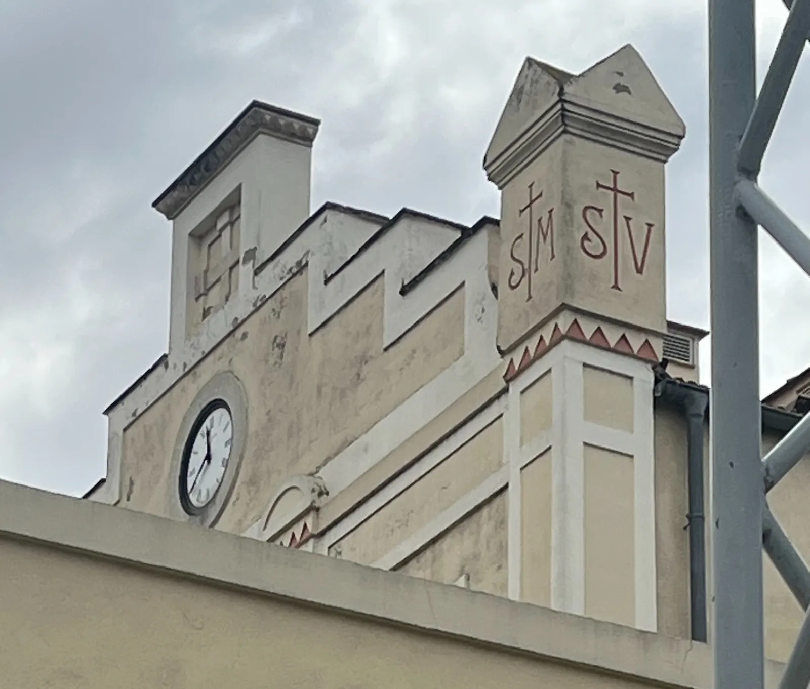 On the facade of a religious, christian building with crosses, and the letters SM and SV, there’s also a clock. It points at 20 to twelve.