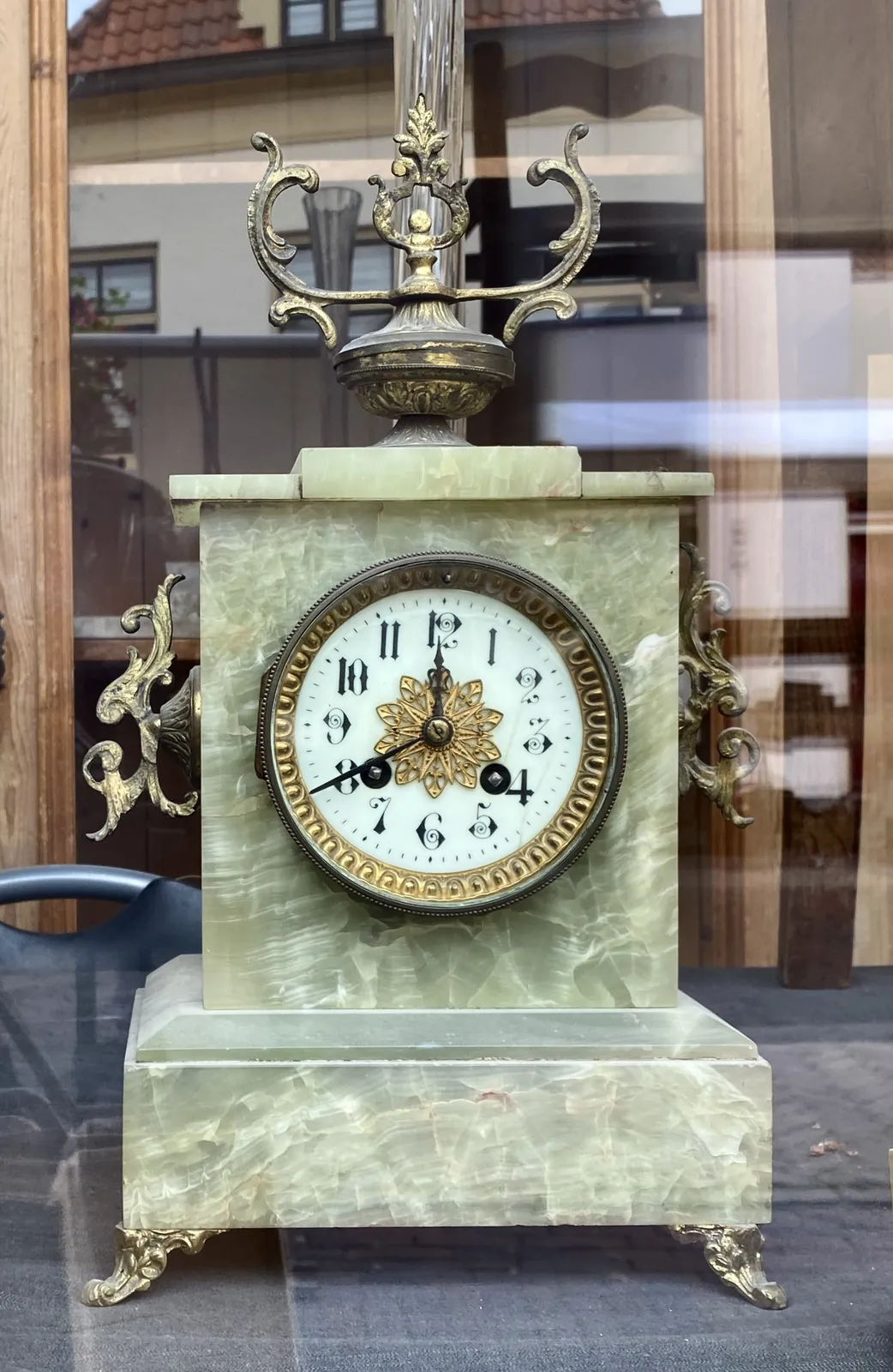 An antique, green marble clock, with elaborate metal ornaments. The clock points at 20 minutes to 12.