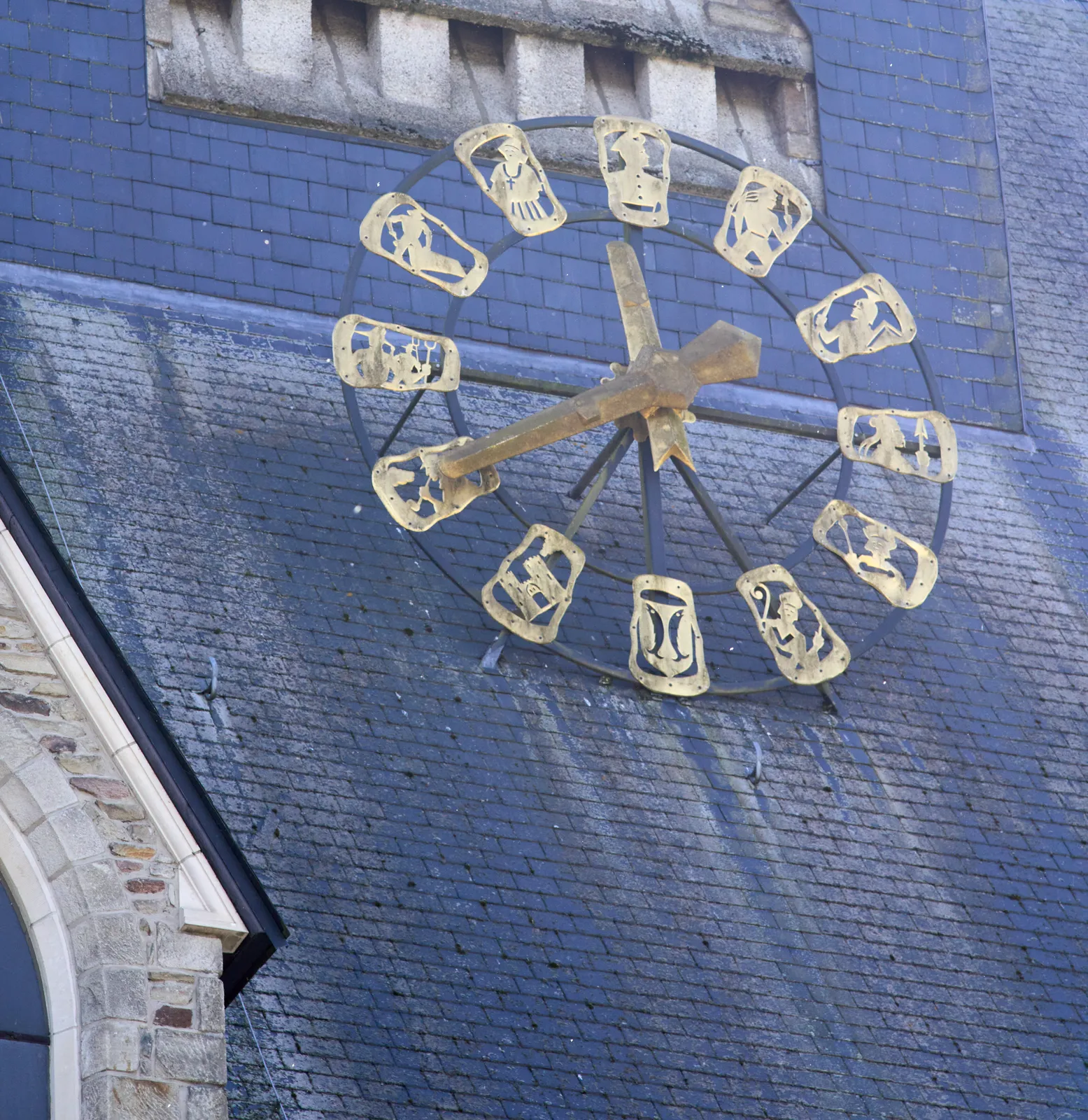 A large golden clock on the roof of a church. The hour indicators are made from golden icons, depicting church life, or something like that. The enormous golden hands point at 20 minutes to twelve. 