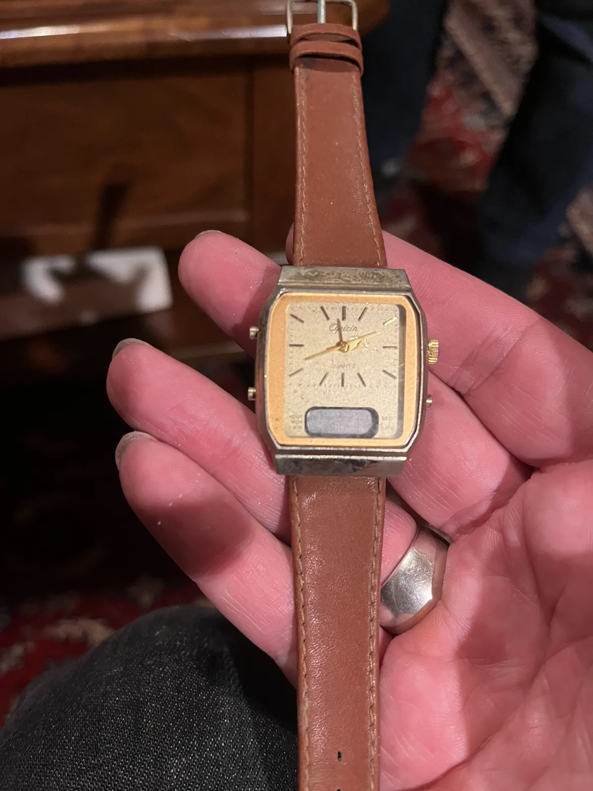 Someone is holding an old watch in their hand. In the background, blurry, an old Persian carpet. The watch points at 18 minutes to twelve.