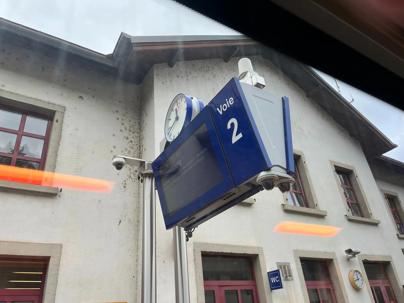 A clock on top of a display that shows that this train will go to Luxembourg. The clock points at 17 minutes to 12. 