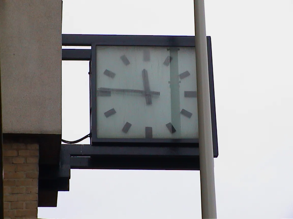 This clock, attached to a building, points at 14 to 12.