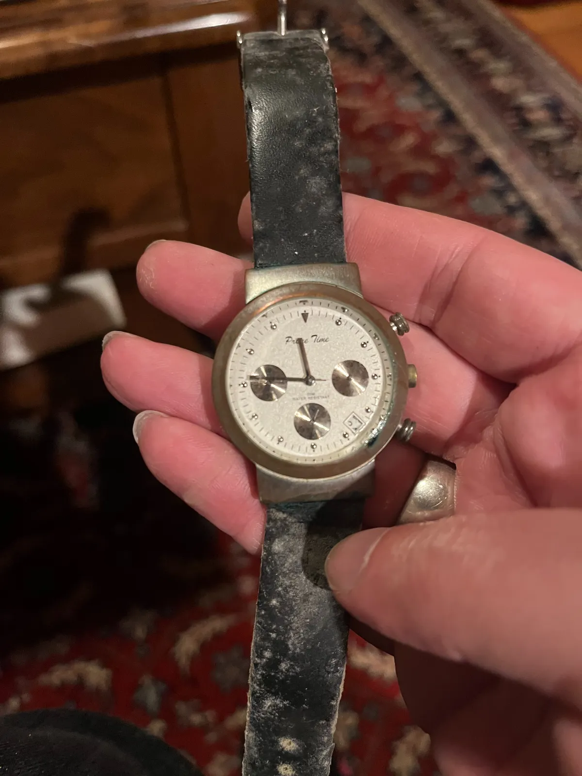 Someone is holding an old watch in their hand. In the background, blurry, an old Persian carpet. The watch points at 14 minutes to twelve.