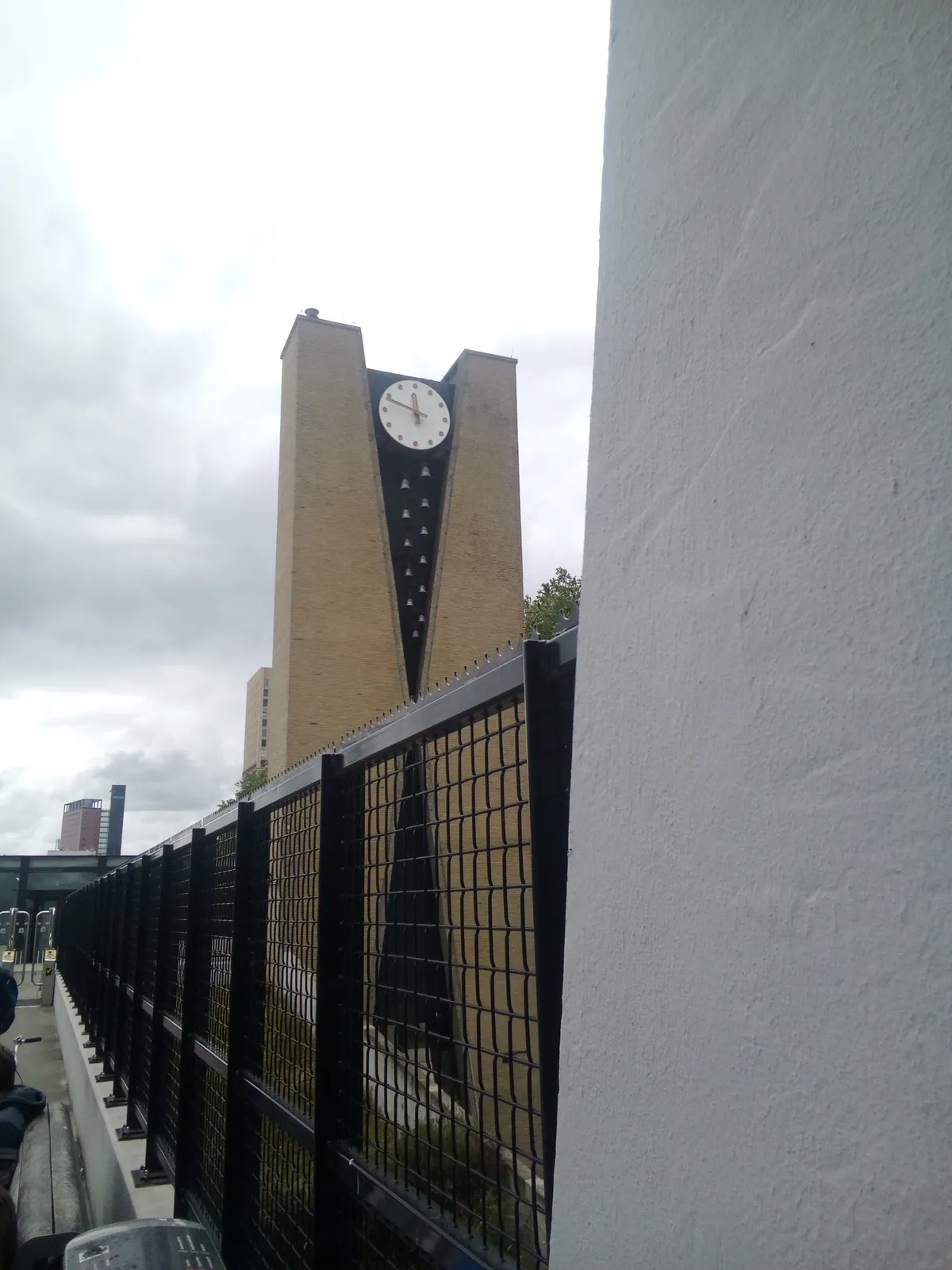A large clock on a large, modern, high brick tower. It points at 11 minutes to twelve.