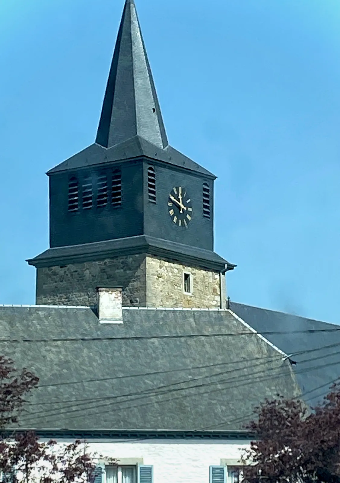 A rather bulky church tower with a clock on it that points at 11 minutes to 12.