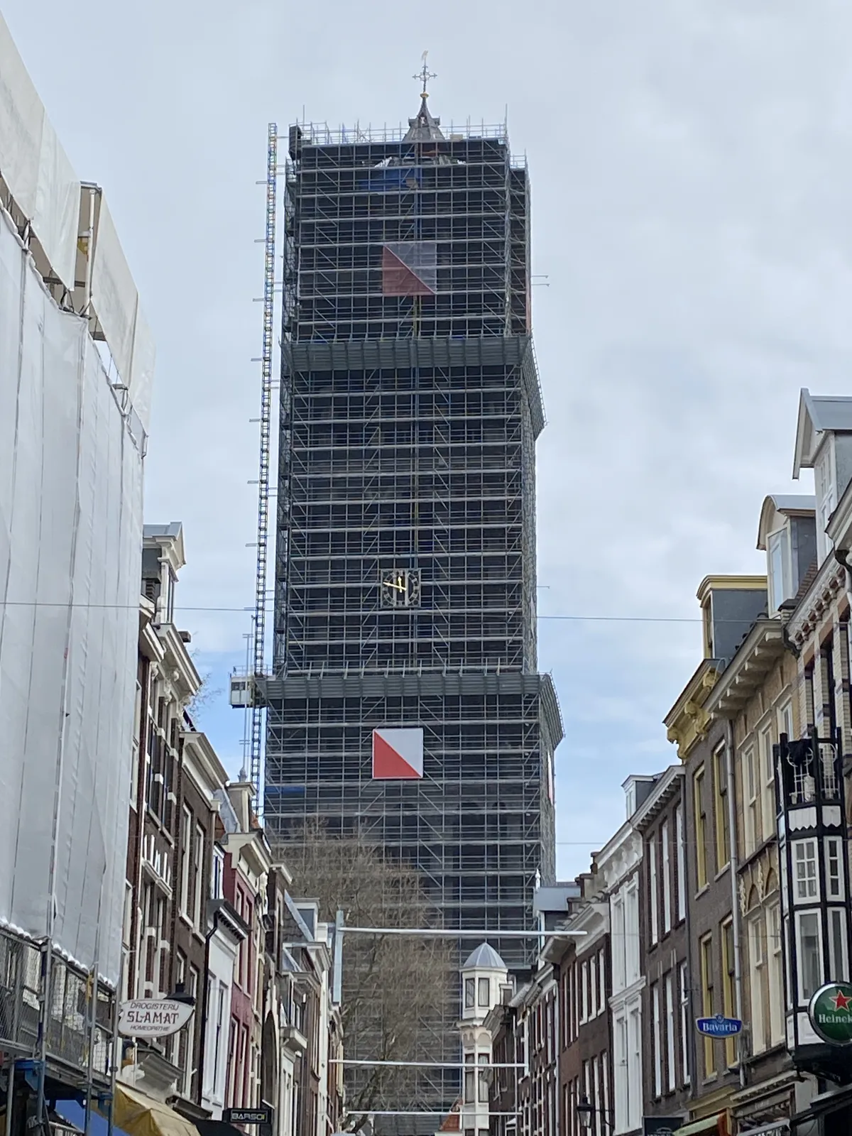 The Dom tower in Utrecht is tightly packed in scaffolding. There’s a church clock attached to the scaffolding and it points at 11 minutes to twelve.