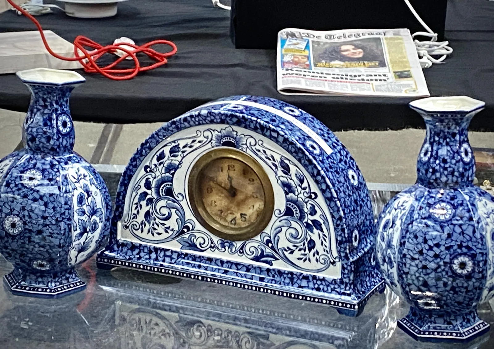 A blue and white, halve oval ceramic clock next to two blue and white ceramic vases. The clock points at 10 minutes to 12.